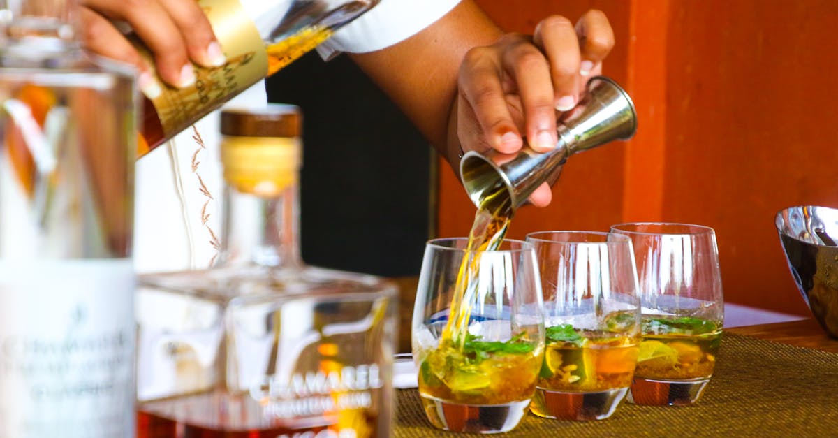 A bartender expertly pours cocktails in glasses on a bar counter.